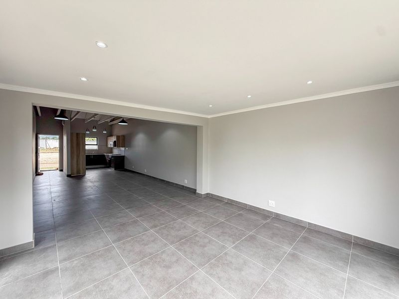 Spacious open-plan living area featuring modern grey floor tiles, recessed lighting, and a seamless transition to a functional kitchen space.