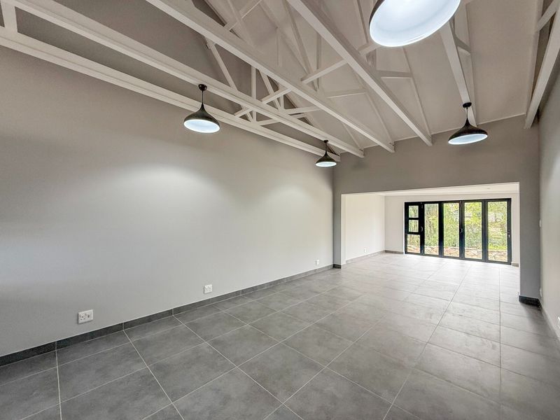 Spacious open-plan living area featuring high ceilings with exposed white trusses, modern tiled flooring, and large bi-fold doors leading to the outdoors.