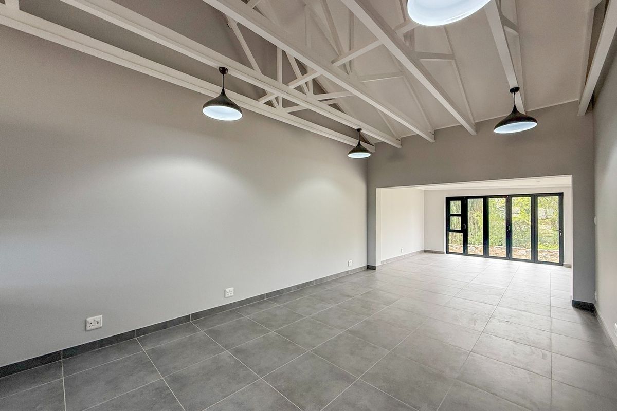 Spacious open-plan living area featuring high ceilings with exposed white trusses, modern tiled flooring, and large bi-fold doors leading to the outdoors.