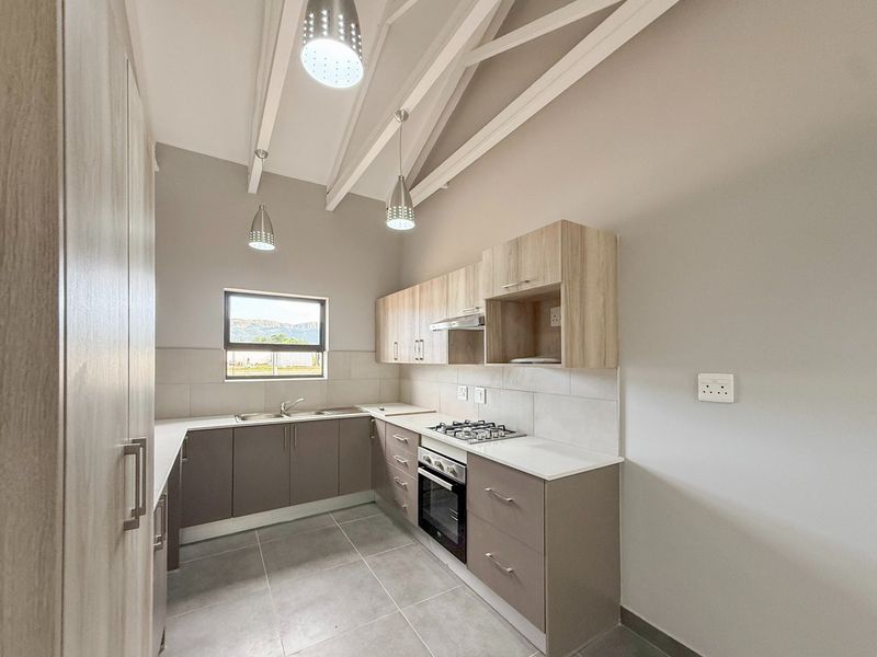 Modern kitchen featuring light wood-tone cabinetry, gas hob, electric oven, tiled splashback, and exposed ceiling beams with pendant lighting.