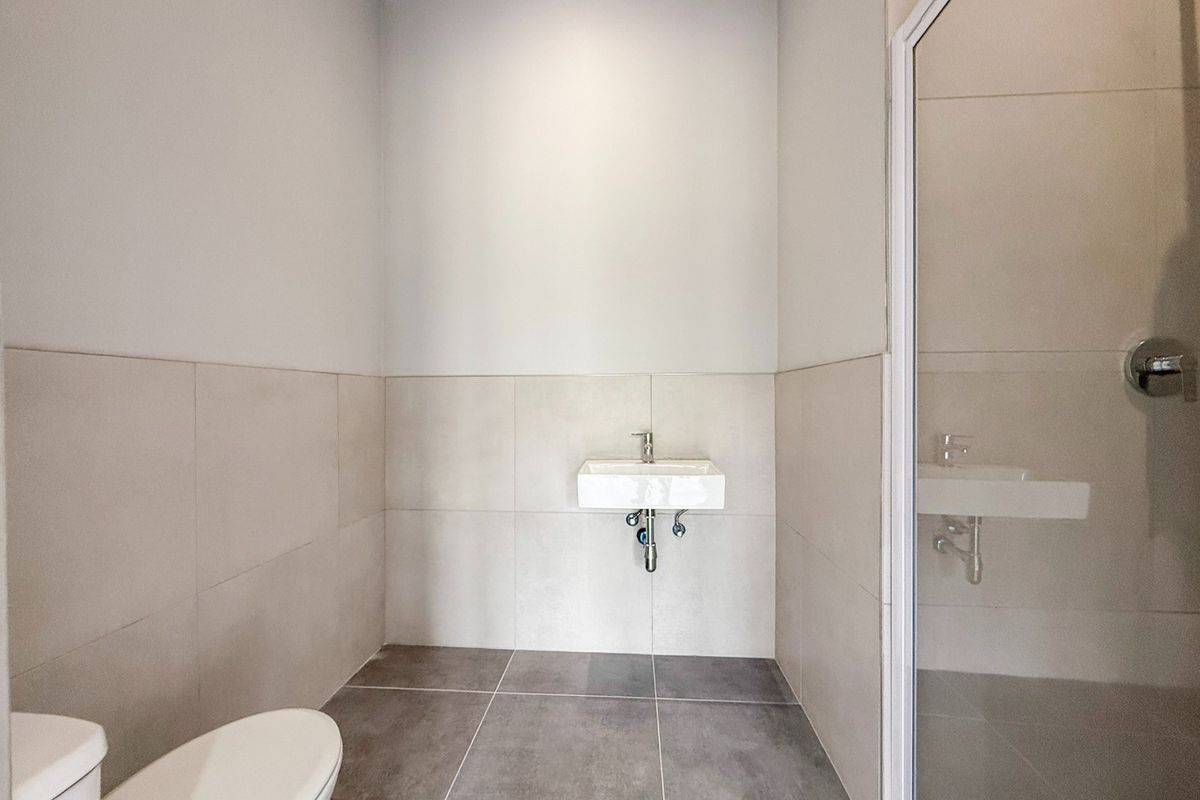 A clean, modern bathroom featuring a wall-mounted basin, toilet, and a glass-enclosed shower with neutral ceramic tiling throughout.