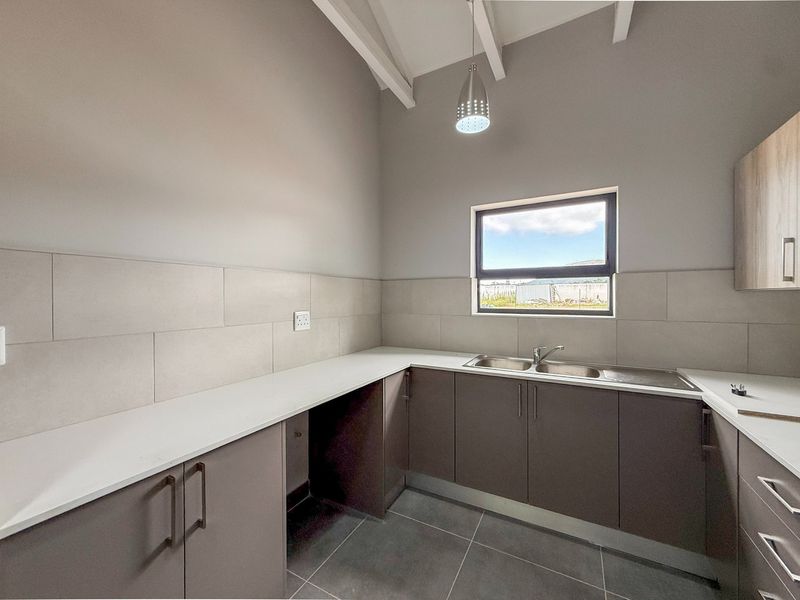 A clean, modern scullery featuring ample cabinetry, stone-look countertops, double sink, and neutral ceramic tiling under exposed timber rafters.