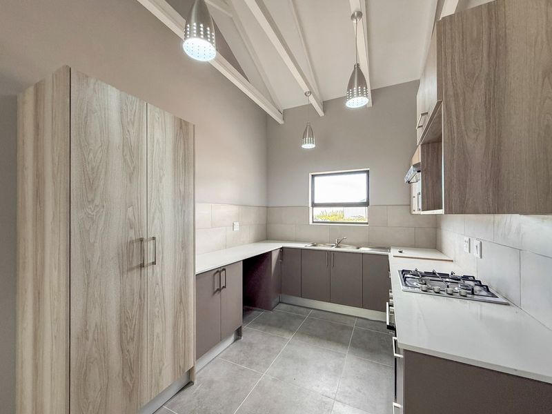 Modern kitchen featuring light wood-tone cabinetry, stone countertops, a gas cooktop, tiled backsplash, and high vaulted ceilings with exposed rafters.