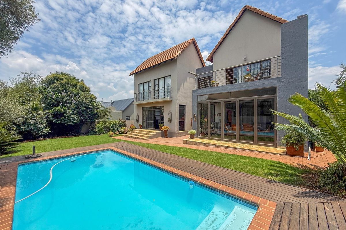 Rear view of the property featuring a swimming pool with timber decking, a landscaped garden, and a multi-level facade with balconies and sliding glass doors.