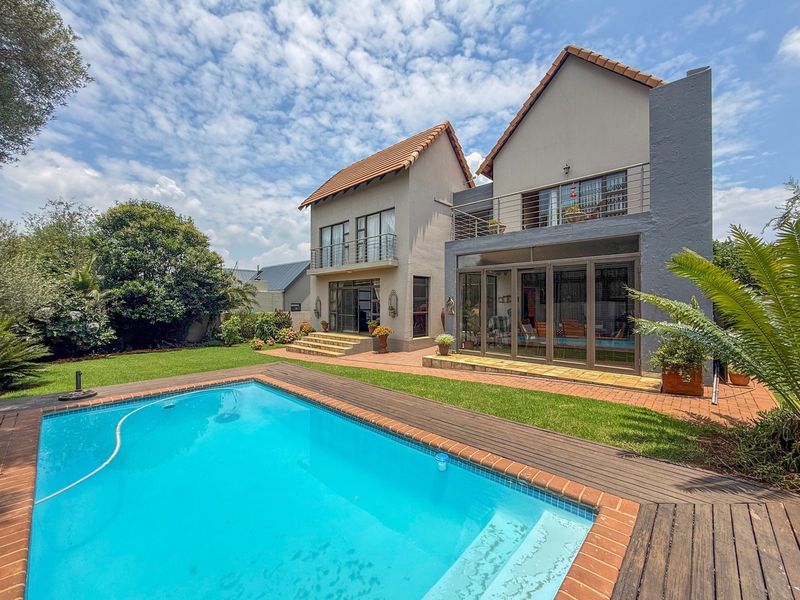 Rear view of the property featuring a swimming pool with timber decking, a landscaped garden, and a multi-level facade with balconies and sliding glass doors.