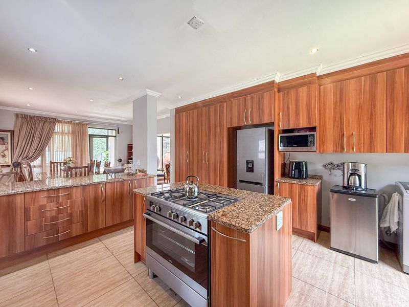 Spacious open-plan kitchen featuring wood veneer cabinetry, granite countertops, and a central island with a gas hob, seamlessly flowing into the dining area.