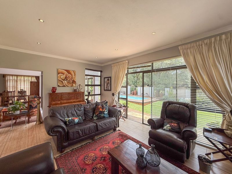 A well-lit living room featuring tiled floors, recessed lighting, and large sliding glass doors providing direct access to the garden and pool area.