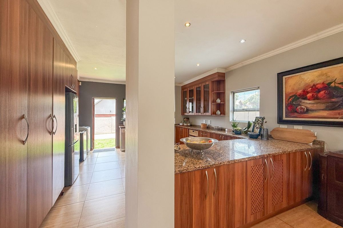 Spacious kitchen featuring warm wood cabinetry, granite countertops, and tiled flooring, with an open-plan layout leading to a rear exterior access point.
