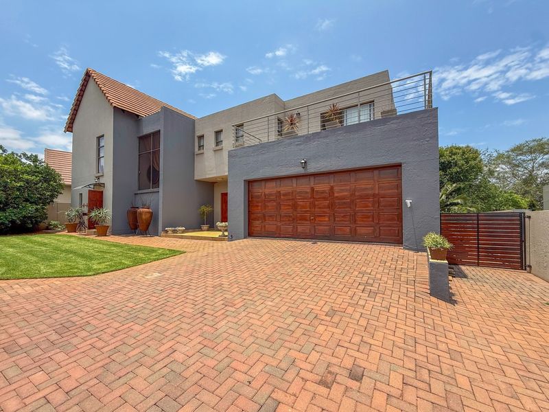 Modern double-storey home featuring a paved driveway, timber garage door, and an upper-level balcony with metal railings.