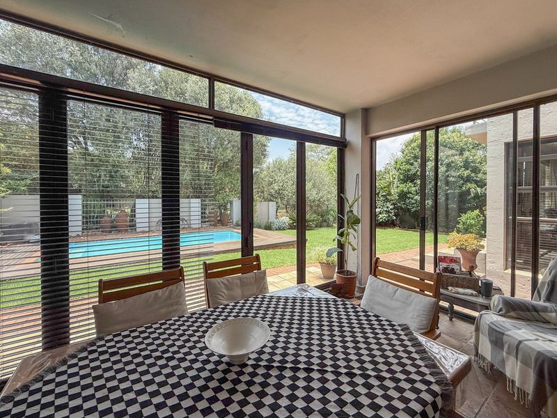 A bright, enclosed patio area featuring extensive glass sliding doors that provide seamless views of the garden and swimming pool.