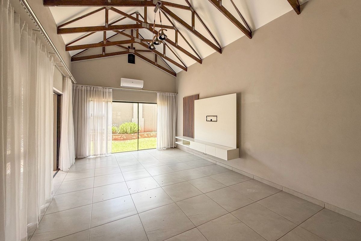 Spacious living area featuring high vaulted ceilings with exposed timber trusses, tiled flooring, and a modern built-in media console with direct garden access.