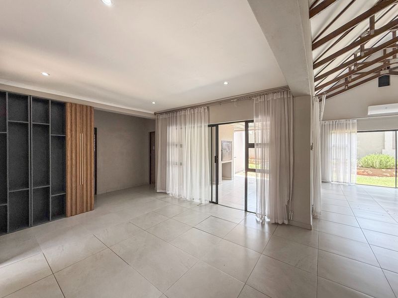 Spacious open-plan living area featuring large format floor tiles, built-in cabinetry, exposed timber trusses, and seamless access to the outdoor patio through sliding glass doors.