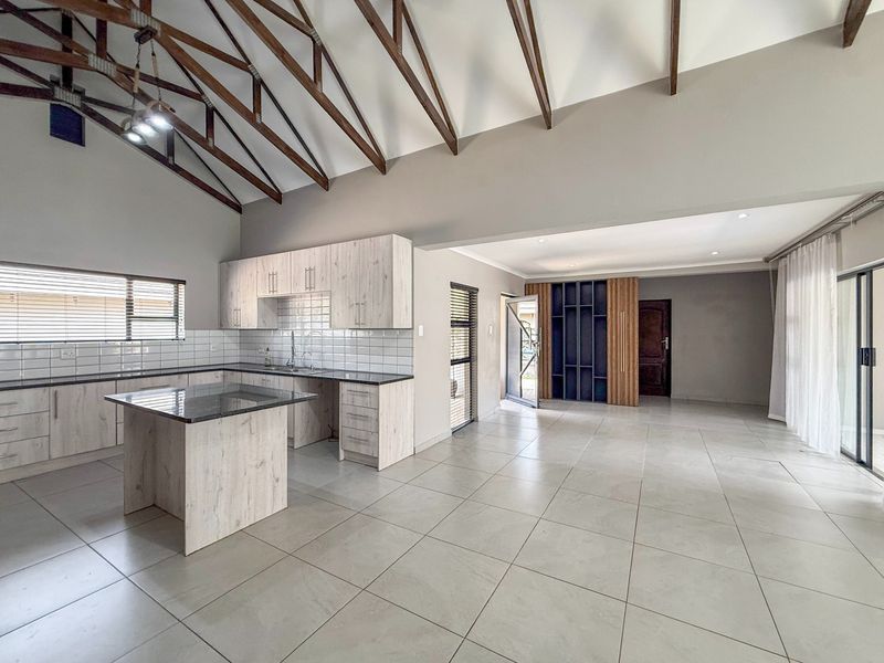 Spacious open-plan kitchen and living area featuring high vaulted ceilings with exposed timber trusses, modern cabinetry, granite countertops, and large sliding doors to the exterior.