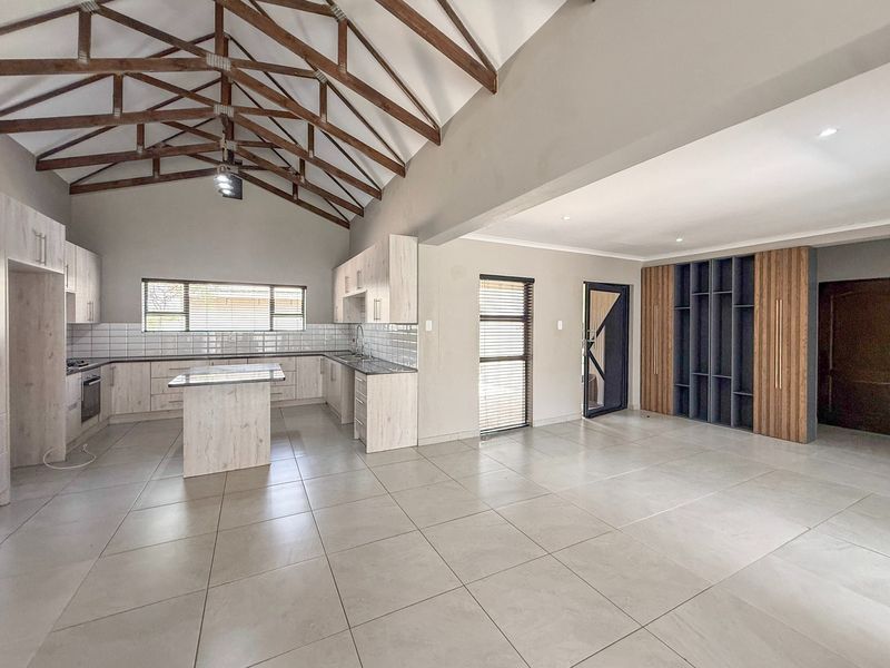 Spacious open-plan living and kitchen area featuring high vaulted ceilings with exposed timber trusses, modern cabinetry, and large format floor tiles.