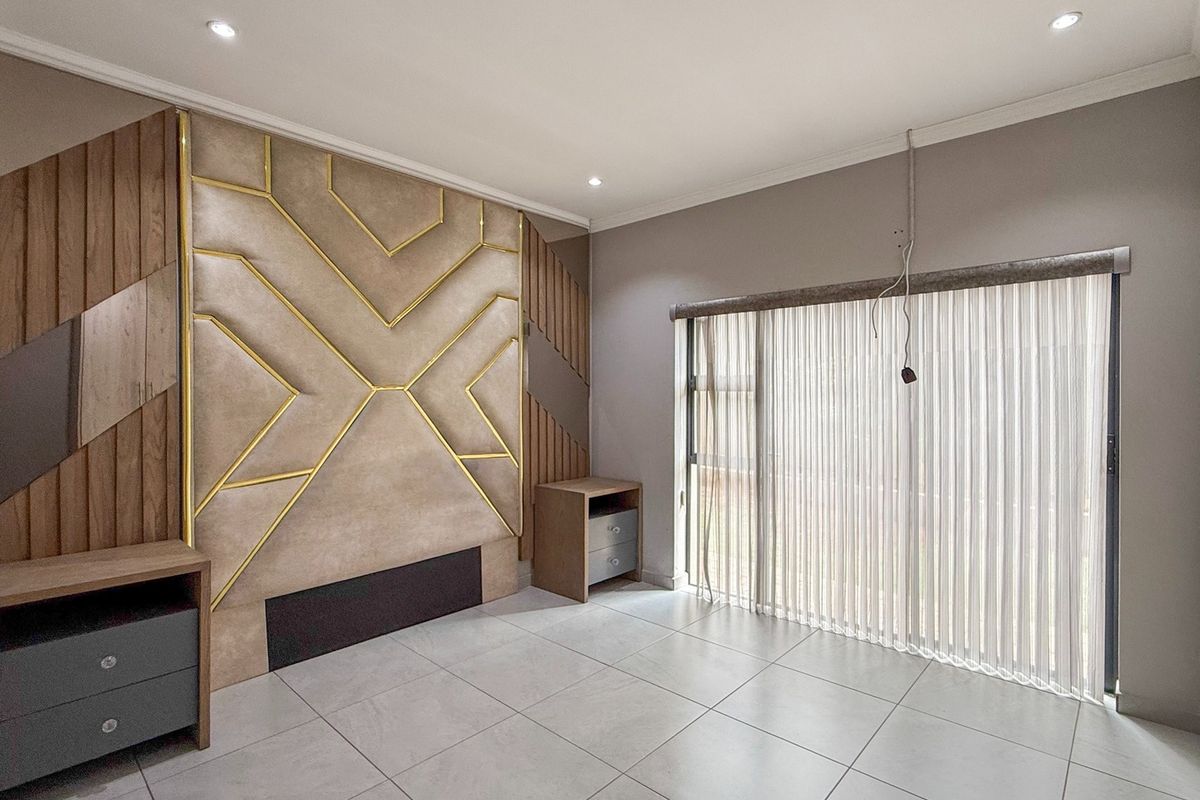 A modern bedroom featuring a decorative upholstered headboard wall, tiled flooring, and a sliding glass door with vertical blinds.