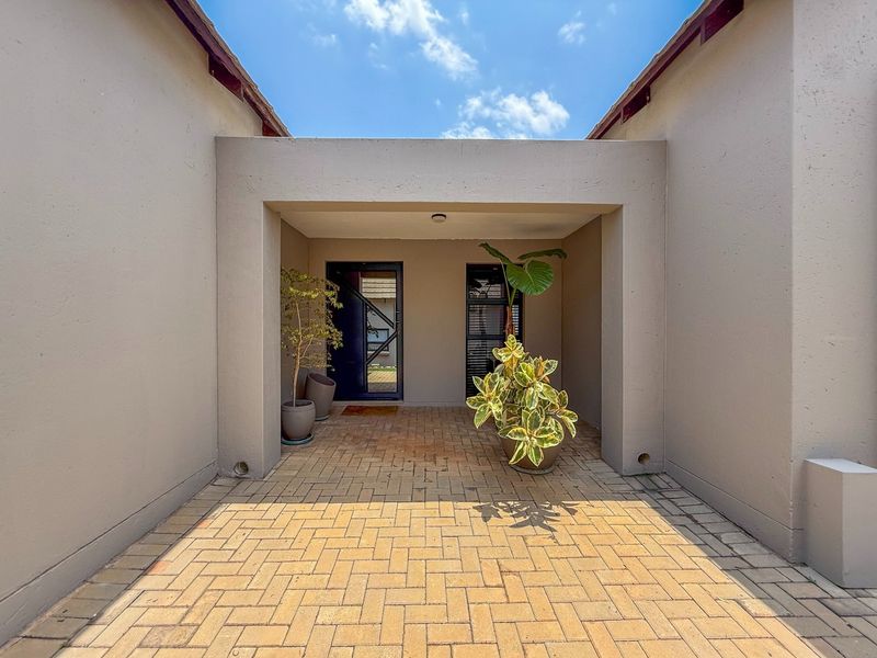 A clean and well-maintained covered entrance area featuring paved flooring and a modern glass-panelled front door.