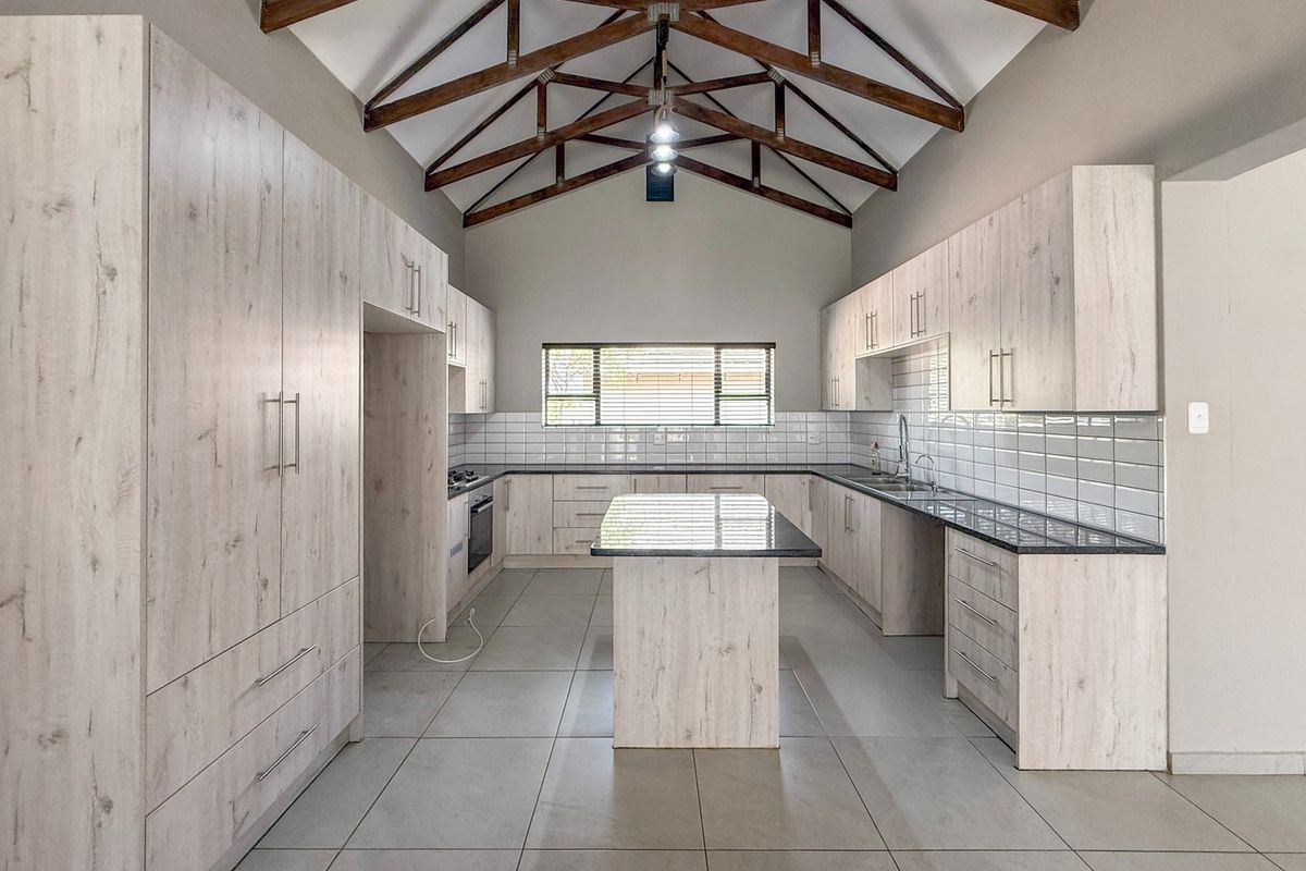 Spacious modern kitchen featuring light wood cabinetry, a central island, subway tile backsplash, and striking exposed timber roof trusses under a vaulted ceiling.