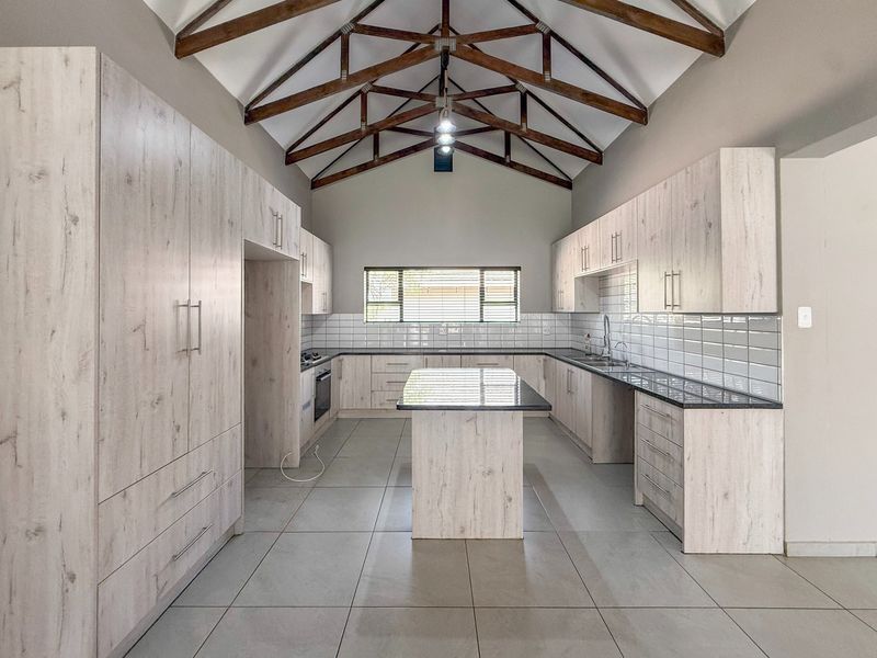 Spacious modern kitchen featuring light wood cabinetry, a central island, subway tile backsplash, and striking exposed timber roof trusses under a vaulted ceiling.