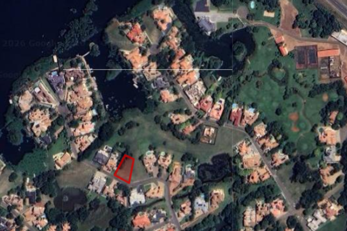 Aerial view of a vacant residential plot highlighted in red, situated within a developed estate with surrounding homes and green spaces.