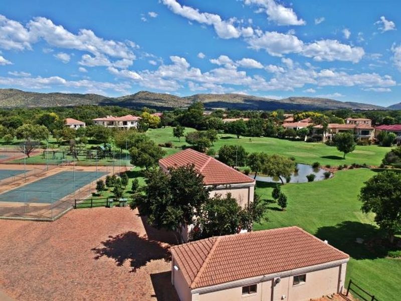 Aerial view of a residential estate featuring tennis courts, a golf course, a pond, and surrounding landscaped grounds.