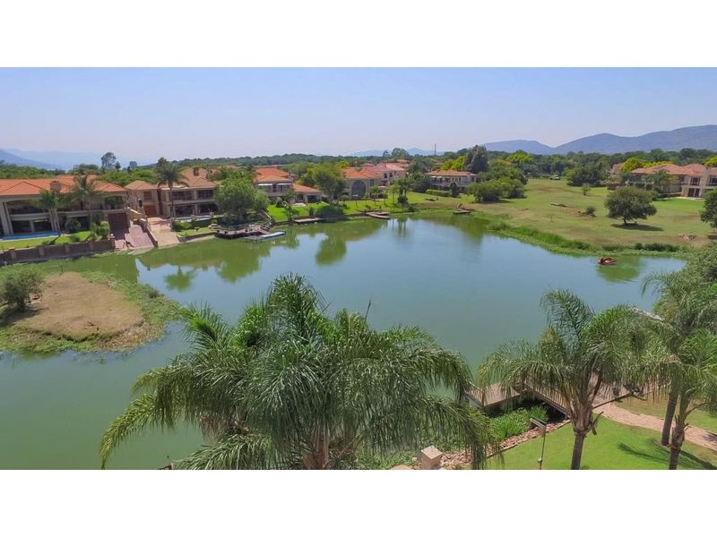 An aerial view of a residential estate featuring a central lake, landscaped grounds, and surrounding properties in a scenic setting.