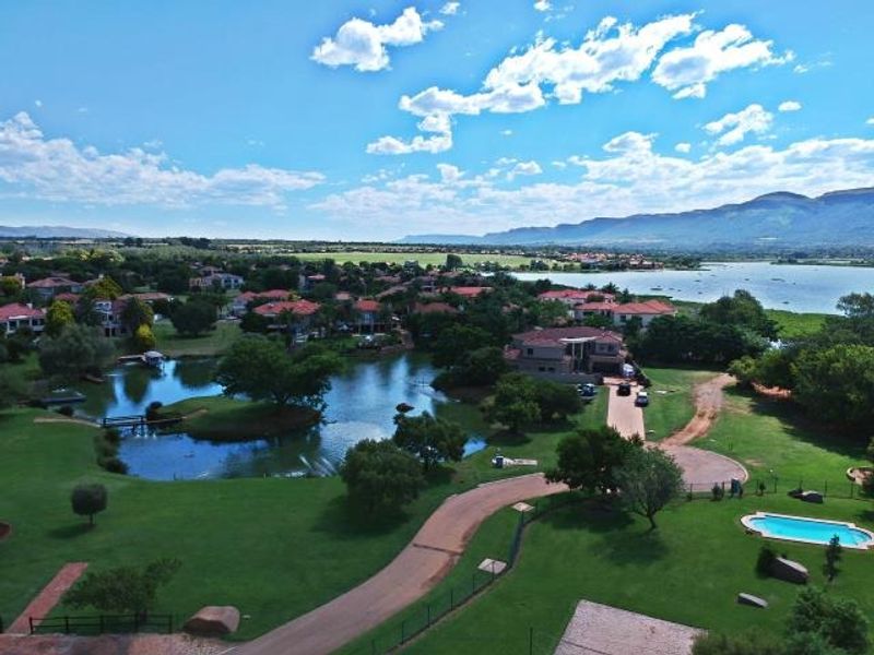 An aerial view of a residential estate featuring a swimming pool, manicured lawns, paved driveways, and scenic lake views with mountain backdrops.