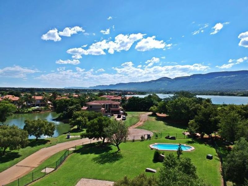 Aerial view of a residential property featuring a swimming pool, expansive green lawns, and scenic views of the surrounding lake and mountains.