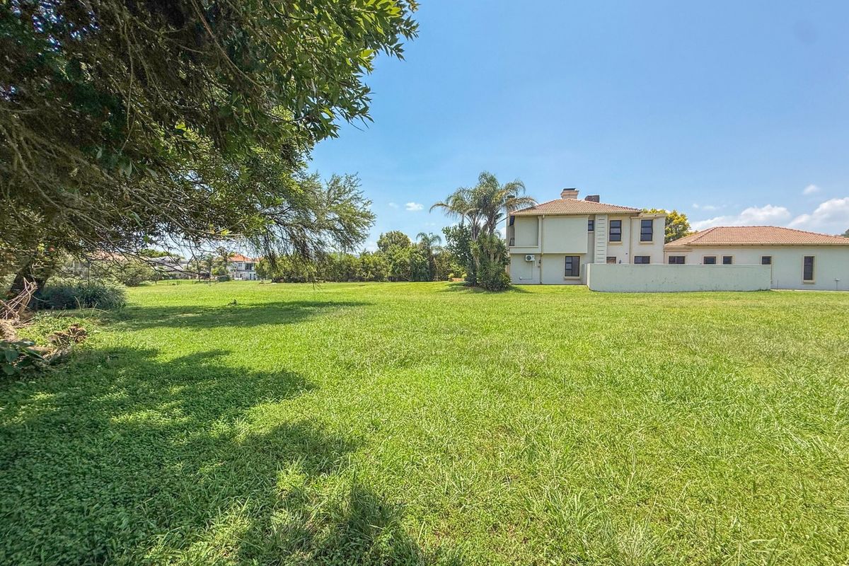 A spacious, well-maintained residential garden featuring a large lawn, mature trees, and a clear view of the adjacent property's rear elevation.