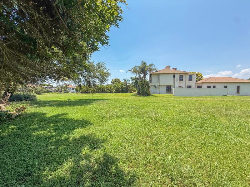 A spacious, well-maintained residential garden featuring a large lawn, mature trees, and a clear view of the adjacent property's rear elevation.