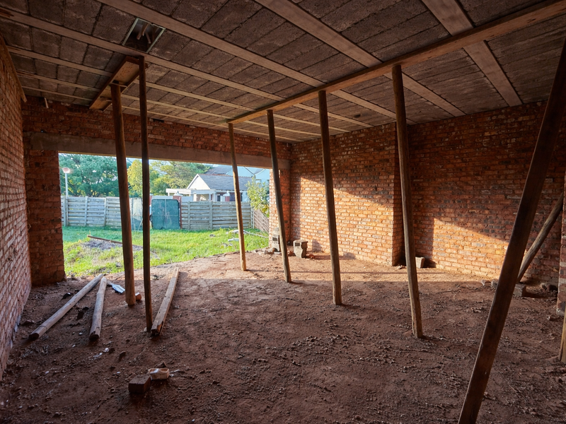 An unfinished interior space featuring exposed brick walls, a concrete slab ceiling, and temporary timber support props, currently in a shell construction state.