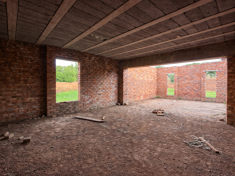 An unfinished open-plan interior space featuring exposed brick walls and a concrete slab ceiling, currently in a shell construction state.