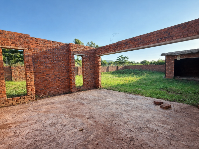 An unfinished brick structure showing the shell of a building under construction with open wall frames and a concrete slab foundation.
