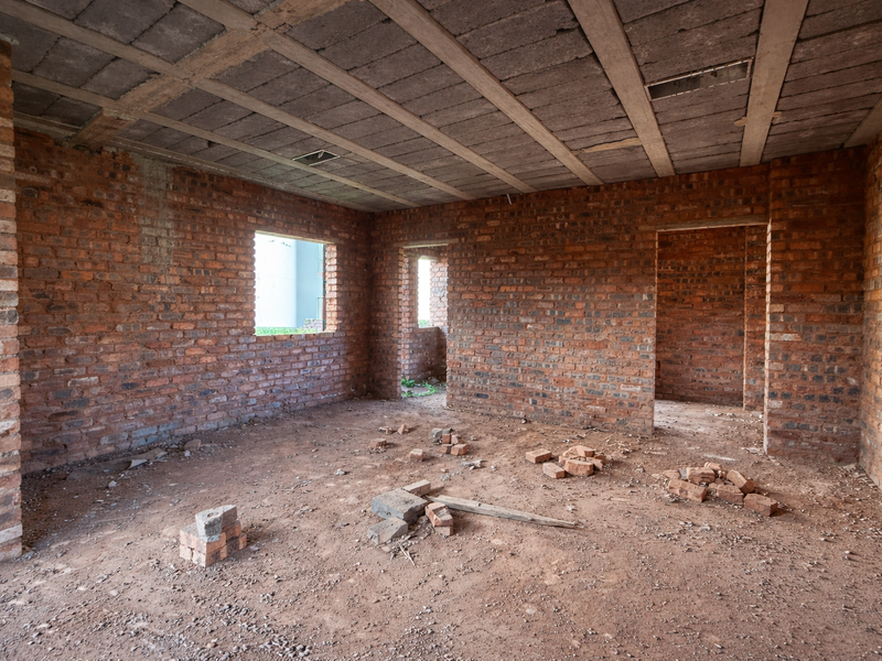 An unfinished interior space featuring exposed brick walls and a concrete slab ceiling, currently in the early stages of construction.