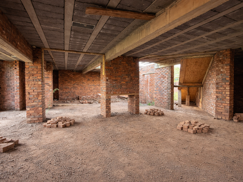 An unfinished interior space featuring exposed brick walls, concrete beam ceilings, and a dirt floor, currently in a shell construction state.