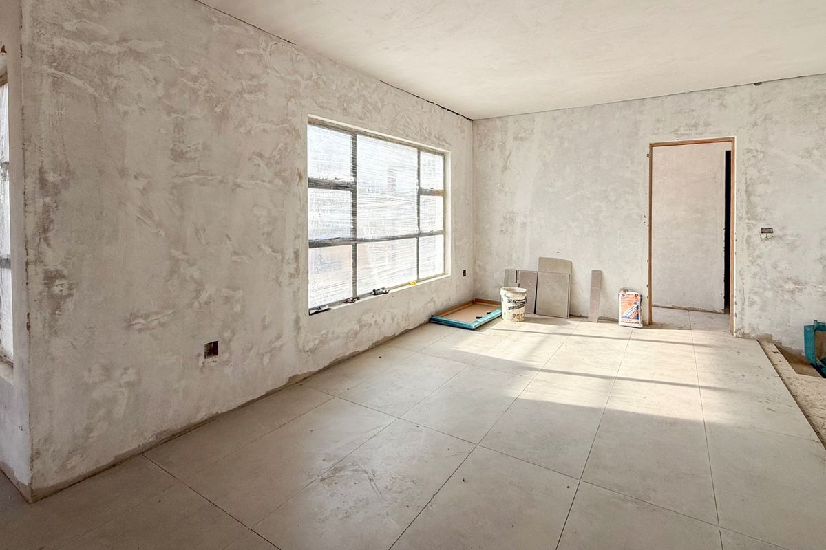 An unfinished living area featuring large windows, tiled flooring, and raw plastered walls, currently undergoing renovation.