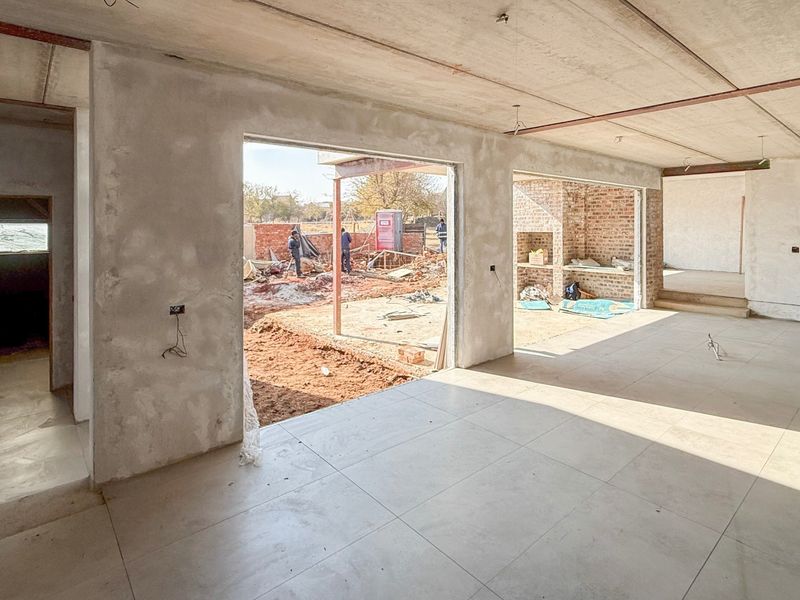 Spacious open-plan living area under construction, featuring large openings to the exterior, tiled floors, and exposed concrete ceilings awaiting final finishes.