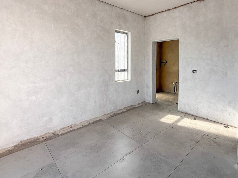 An unfinished bedroom interior featuring tiled flooring and plastered walls, currently in a shell condition awaiting final finishes and trim.