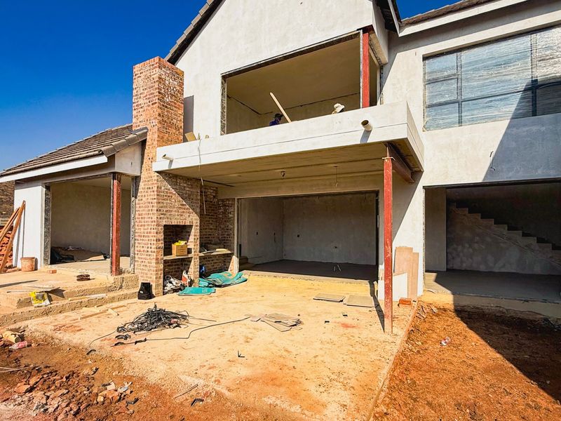 Rear view of a residential property currently under construction, featuring an exposed brick chimney, concrete balcony, and unfinished structural elements.