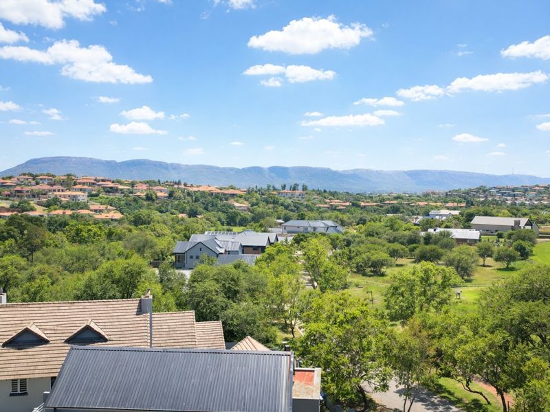 Elevated panoramic view overlooking a lush green residential estate with mountain ranges in the distance.