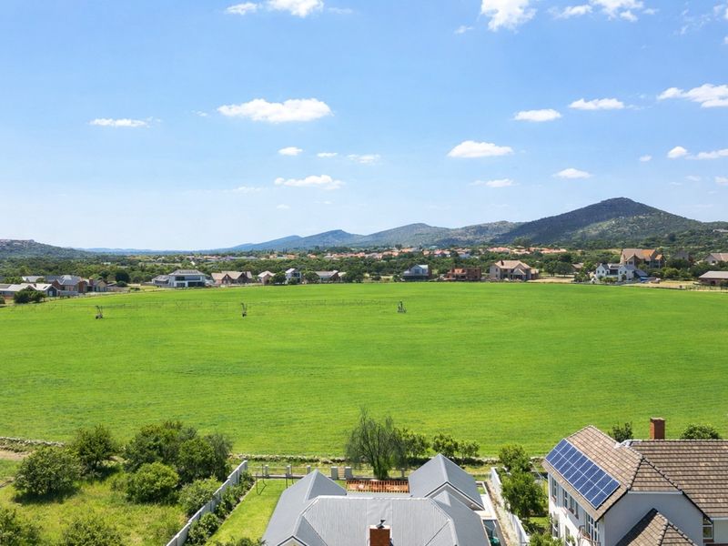 An elevated view overlooking a large green field with residential houses and mountains in the background.