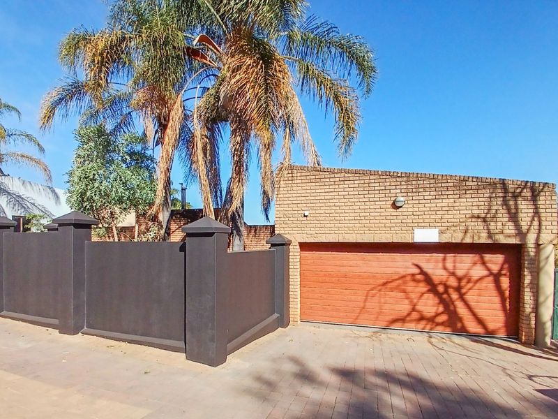 Front view of the property featuring a paved driveway, a secure sectional garage door, and a solid brick boundary wall.