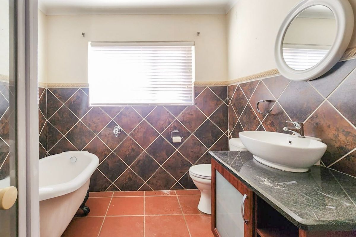 A functional bathroom featuring a freestanding bathtub, a vessel sink on a vanity cabinet, and dark decorative wall tiling.