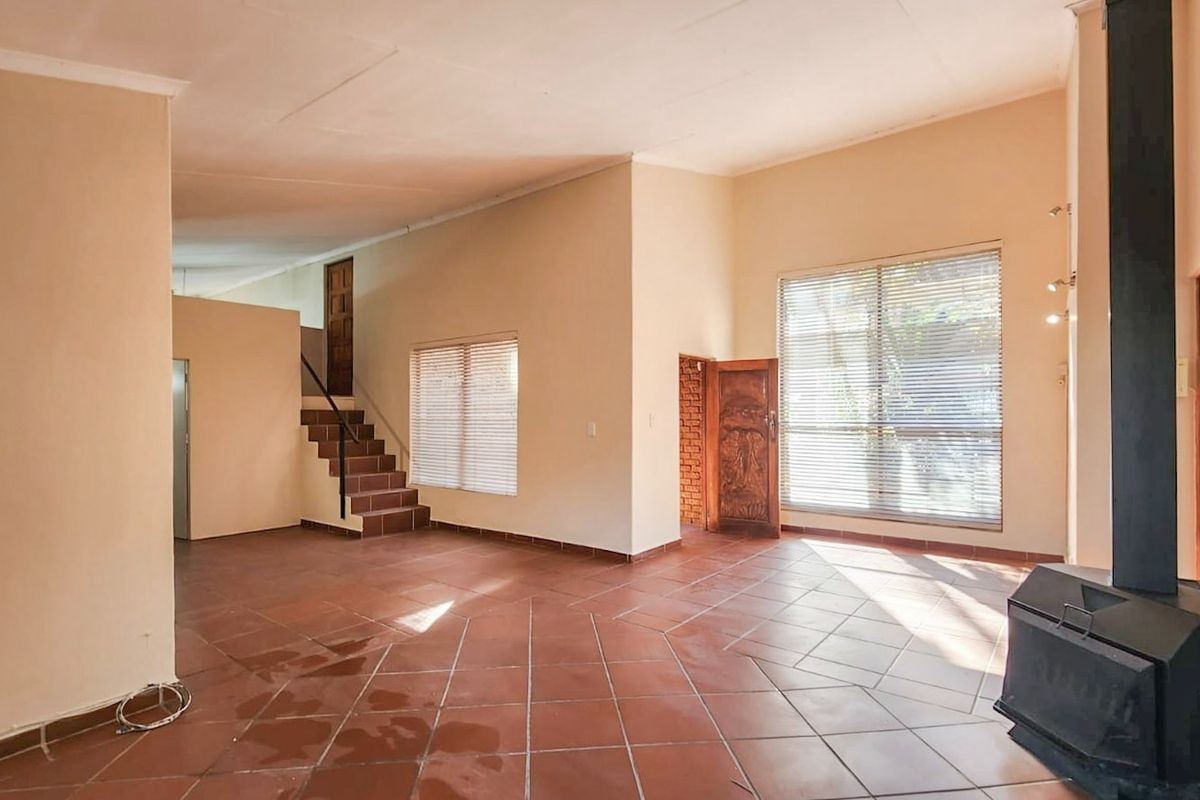 Spacious living area featuring terracotta tiled flooring, a built-in staircase, and a freestanding fireplace, offering a versatile layout with natural light.