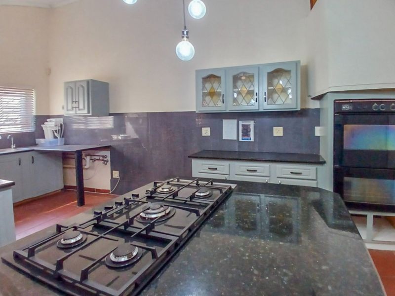 A functional kitchen featuring a central island with a gas hob, granite countertops, built-in oven, and ample cabinetry with a tiled splashback.