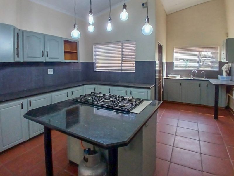 Spacious kitchen featuring a central island with a gas hob, granite countertops, ample cabinetry, and tiled flooring throughout.