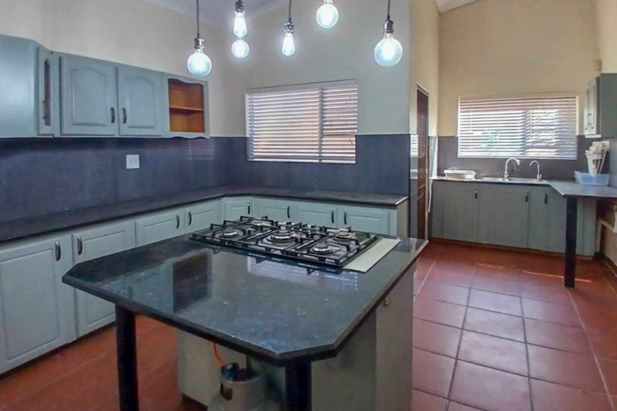 Spacious kitchen featuring a central island with a gas hob, granite countertops, ample cabinetry, and tiled flooring throughout.
