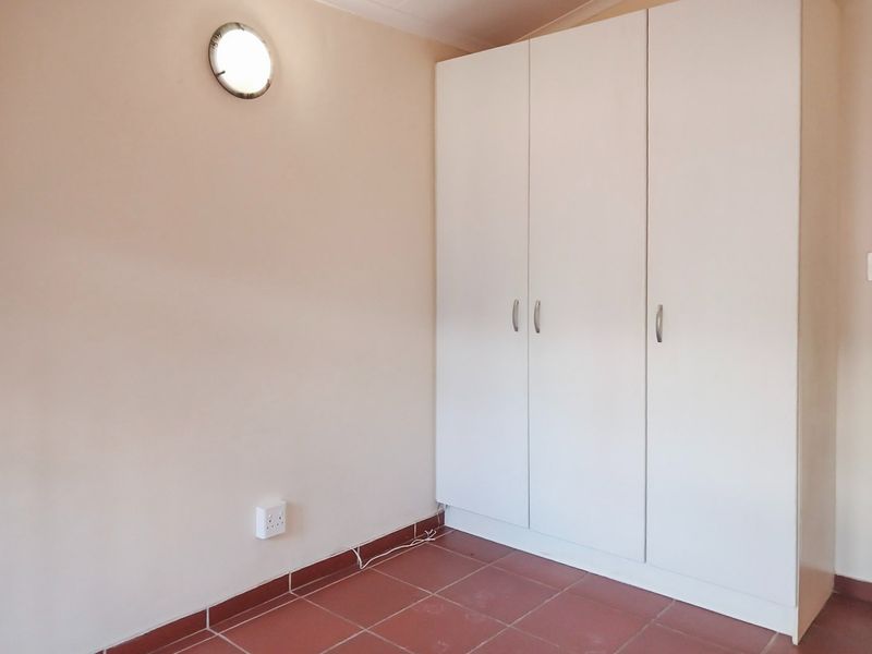 A clean, empty bedroom featuring neutral walls, tiled flooring, and a functional white built-in wardrobe with ample storage space.