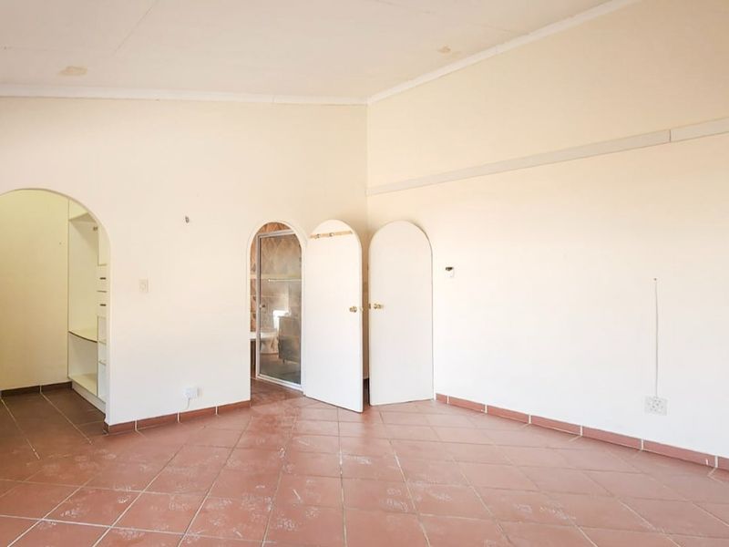 Spacious, empty bedroom featuring tiled flooring, arched doorways leading to an en-suite bathroom and walk-in closet area, and neutral wall finishes.