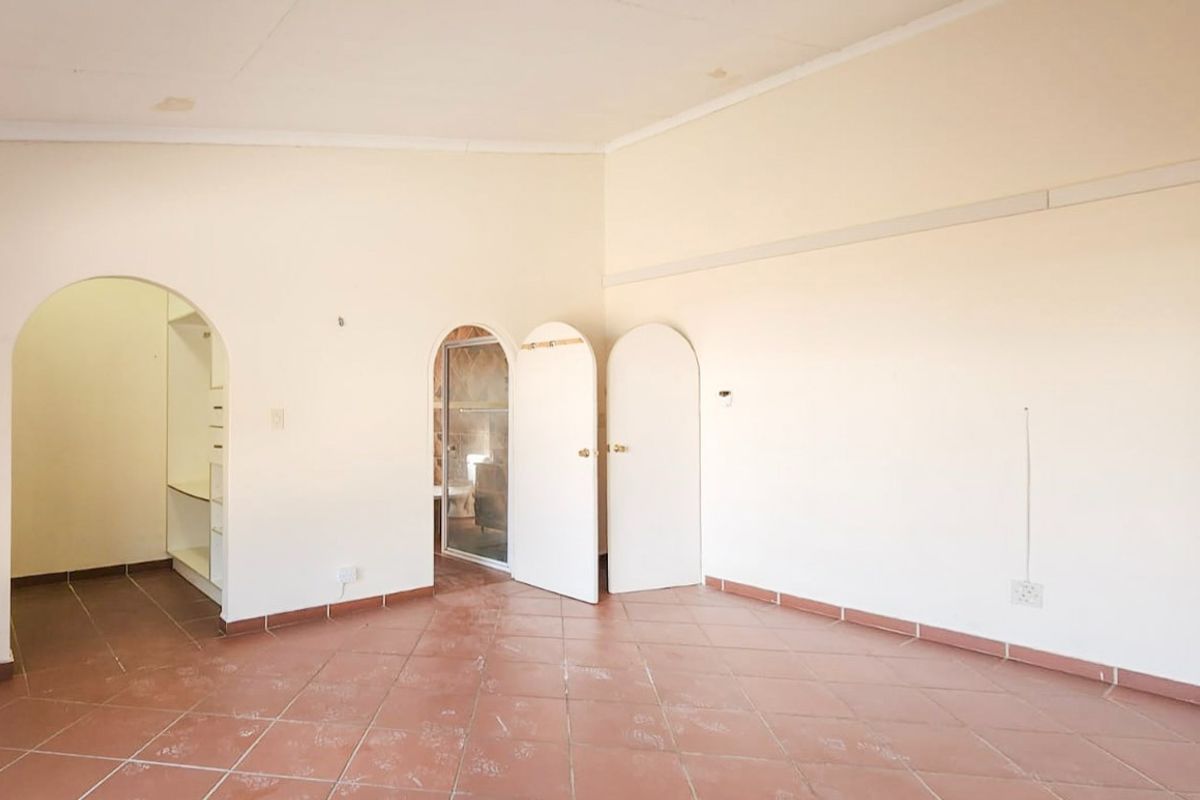 Spacious, empty bedroom featuring tiled flooring, arched doorways leading to an en-suite bathroom and walk-in closet area, and neutral wall finishes.