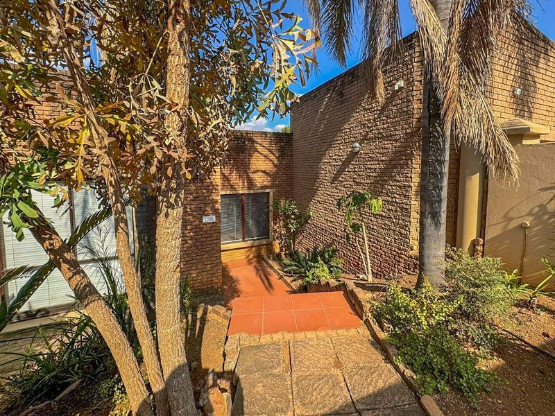 Front entrance area featuring a face brick facade, tiled walkway, and stone paving, surrounded by established garden landscaping.